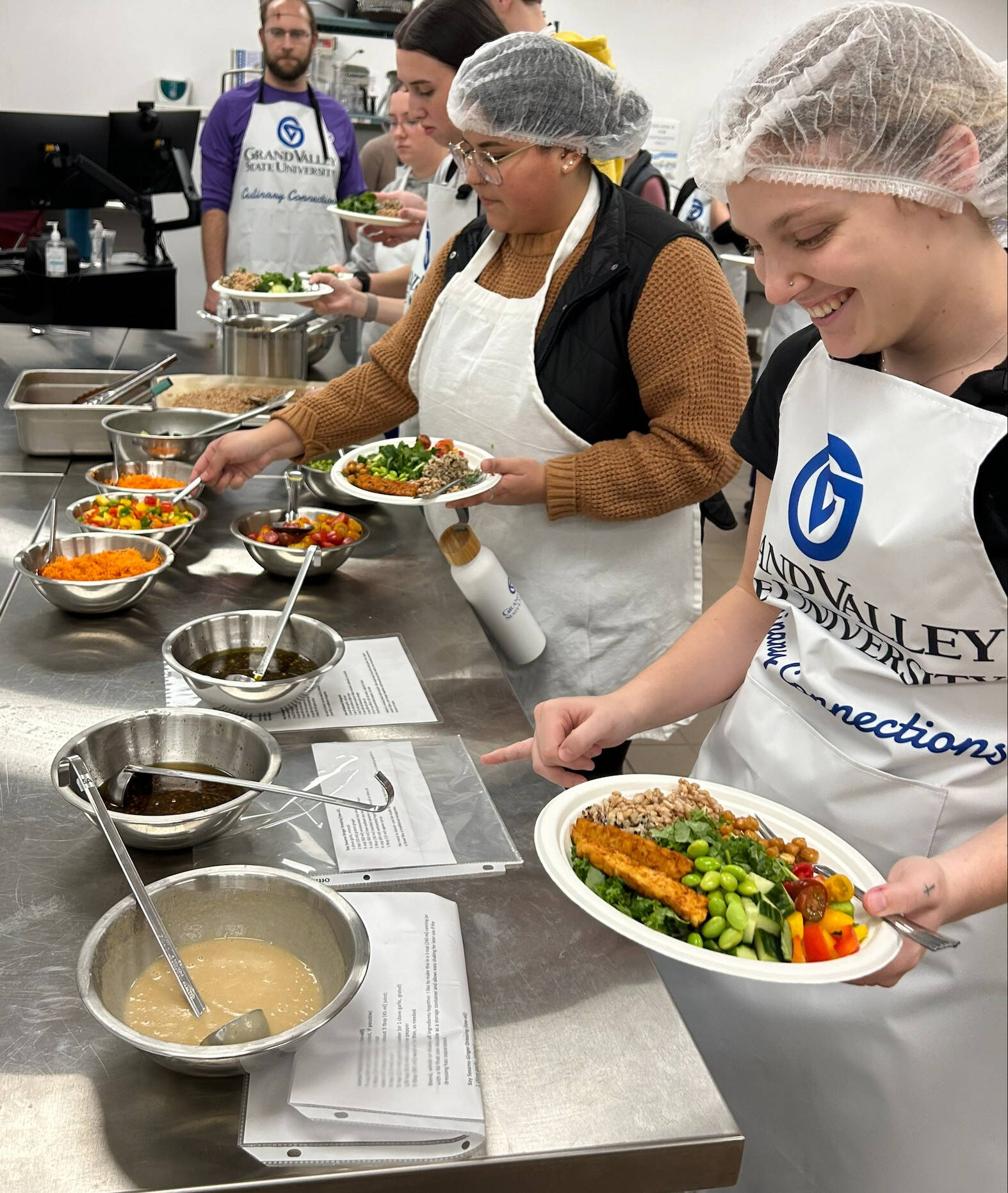Applied Food and Nutrition students, wearing aprons and hair nets, work in the GVSU Culinary Kitchen laboratory.